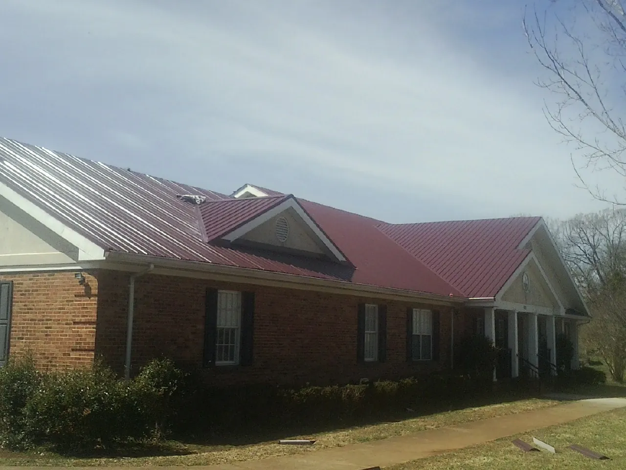 Red metal roof with gabled entries on a long brick building, from a Hail Damage Roof Repair job in Brighton